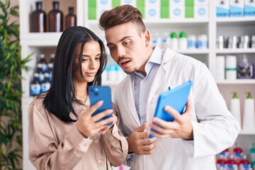 Man and woman pharmacist and client using smartphone and touchpad at pharmacy