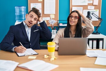 Young hispanic man and woman working at the office stressed and frustrated with hand on head, surprised and angry face