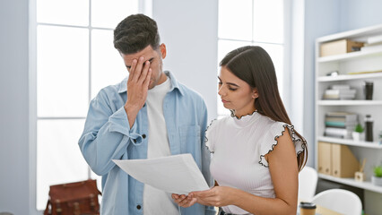 A concerned man and focused woman coworkers review documents together in a bright modern office interior.