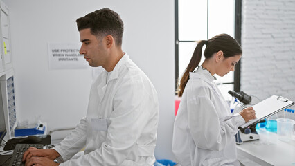 Man and woman scientists working together in a modern laboratory, analyzing data and taking notes.