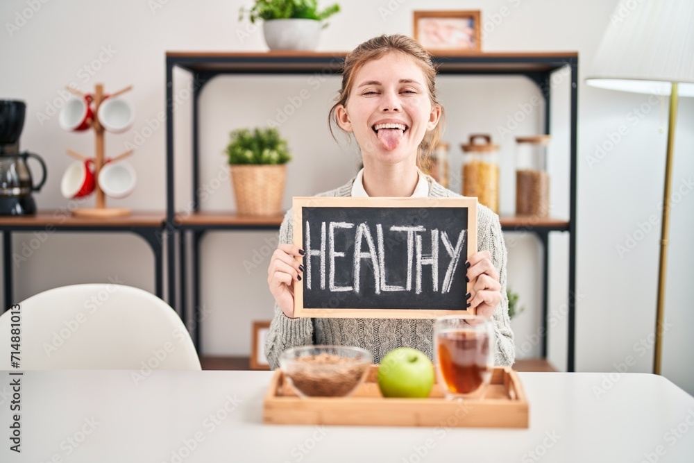 Sticker happy, young blonde woman sticking tongue out in fun, at home, making breakfast. healthy food on bla