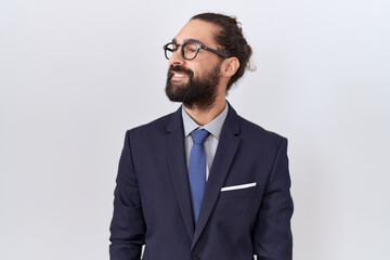 Hispanic man with beard wearing suit and tie looking away to side with smile on face, natural...