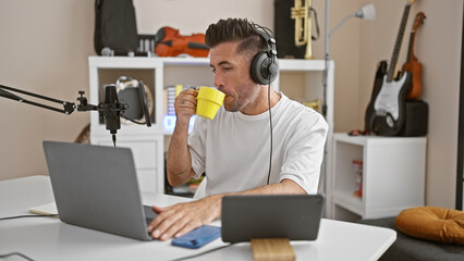 Attractive young hispanic man, a professional reporter, passionately speaking on air in a cozy radio studio, holding a cup of coffee