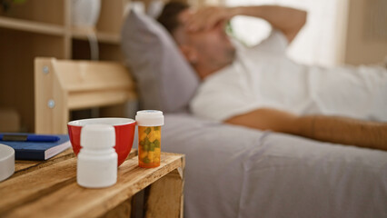 Worried young hispanic man, laid up in bed with a throbbing headache, surrounded by a sea of pills...
