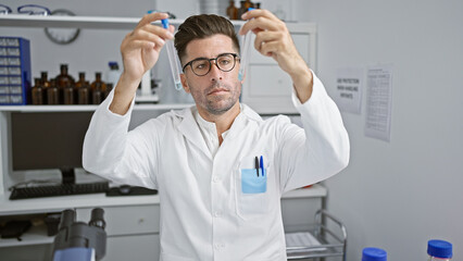 Handsome young hispanic scientist deep in thought, looking at test tubes, working passionately in...