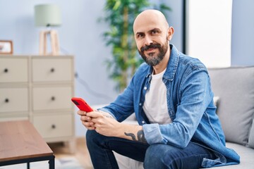 Young bald man using smartphone sitting on sofa at home