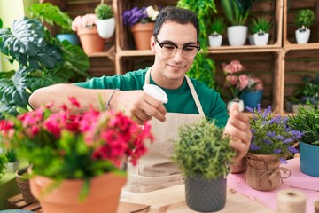 Young hispanic man florist using diffuser watering lavender plant at flower shop
