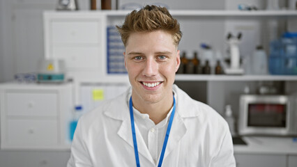 Smiling confident caucasian young man, a handsome scientist, sitting in his lab enjoying the research work. indoors, surrounded by test tubes, a microscope - totally in his element!