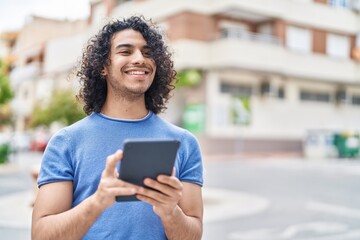 Young latin man smiling confident using touchpad at street