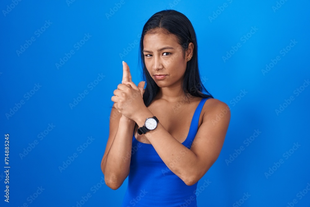 Canvas Prints Hispanic woman standing over blue background holding symbolic gun with hand gesture, playing killing shooting weapons, angry face