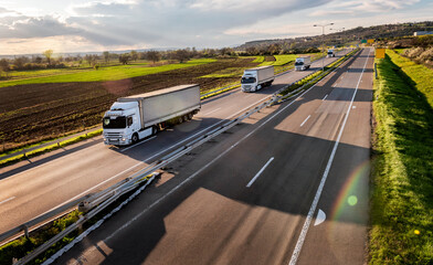Highway transportation scene with Convoy of transportation trucks in line on a rural highway under a beautiful sunset sky