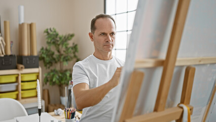 Fototapeta premium Concentrated middle age man artist passionately drawing in studio, immersed in creativity with brush, canvas and palette