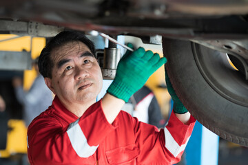 Male car mechanic worker working underneath lifted car. Asian male mechanic vehicle service...