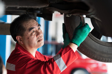 Male car mechanic worker working underneath lifted car. Asian male mechanic vehicle service maintenance checking under car condition in garage. Auto car repair service and maintenance concept