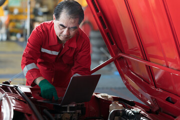 Senior Asian male mechanic checking engine car with laptop computer in auto repair shop. Male...
