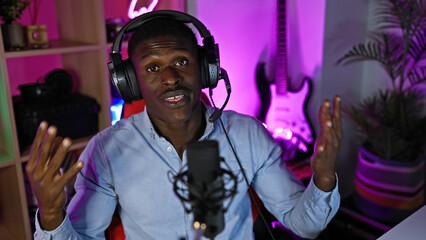 African man podcasting with microphone and headphones in a neon-lit gaming room at night