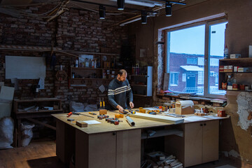 A carpenter works in a furniture workshop with various tools and a board