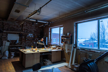 A carpenter works in a furniture workshop with various tools and a board