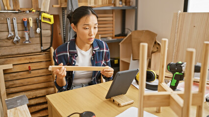 Asian woman carpenter analyzing wood in workshop during videocall