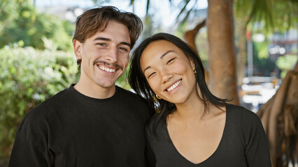 Fototapeta na wymiar Smiling interracial couple, chinese woman and hispanic man, embracing in a lush park