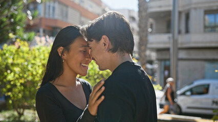 A loving interracial couple embrace happily outdoors on a sunlit city street, depicting a romantic...