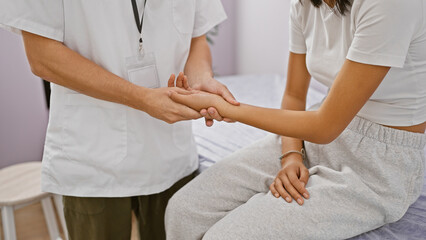 Fototapeta premium Physiotherapist in white uniform examines female patient's hand in a clinic room indoors.