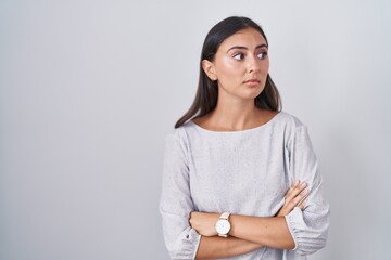 Young hispanic woman standing over white background looking to the side with arms crossed convinced and confident - obrazy, fototapety, plakaty