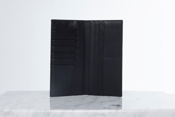Dark leather wallet for credit cards and money on marble floor and white backdrop in studio