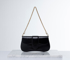 Black, shiny leather bag with gold chain, on a marble floor and white background in the studio