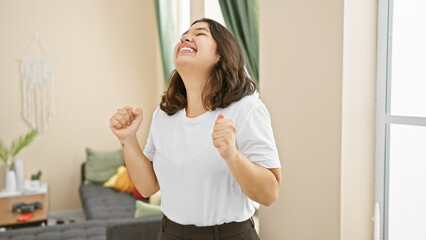Laughing young hispanic woman celebrating joyfully in a cozy home interior.
