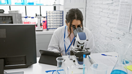 Hispanic woman scientist using microscope in laboratory setting