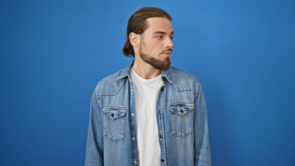 Young hispanic man looking to the side with serious expression over isolated blue background