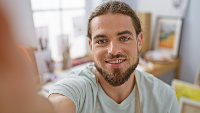 Young hispanic man artist taking selfie picture smiling at art studio
