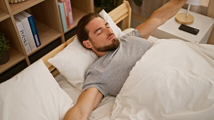 Young hispanic man waking up stretching arms at bedroom