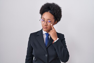 Beautiful african woman with curly hair wearing business jacket and glasses pointing to the eye...
