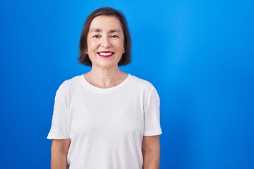 Middle age hispanic woman standing over blue background with a happy and cool smile on face. lucky person.