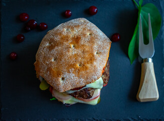 Homemade bacon cheeseburger on a dark tile with berries on the side. Food porn and nasty burger, smash burger from above