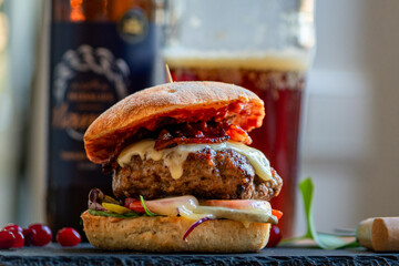 Homemade bacon cheeseburger on a dark tile with berries on the side and cold beer in the background. Food porn and nasty burger, smash burger