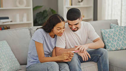 Beautiful couple, beaming with joy, holding positive pregnancy test relaxing at home, radiating...
