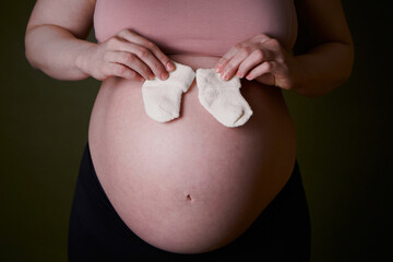 A pregnant woman holds baby socks on her big belly. Fertilization, pregnancy, women's consultation,...