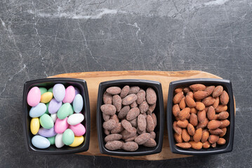 Three varieties of almonds in a black bowls on a olive wood board with a marbled background.