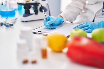 Young beautiful hispanic woman scientist writing food and pills report at laboratory