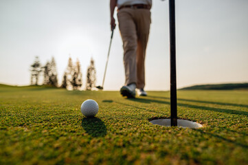 green, golf, ball, club, course, golfer, grass, sport, golfing, fairway. blurred golfer putting ball on the green golf, lens flare on sunset evening time. Golfer putting golf ball near the hole.