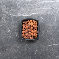 Salted almonds in a black bowl on a marbled surface.