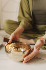 Close up photo of woman hands holding playing on Tibetan singing bowl while sitting on yoga mat. Vintage tonned. Soft focus, blurred and noise effect