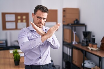 Young hispanic man at the office rejection expression crossing arms doing negative sign, angry face