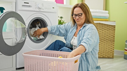 Middle age hispanic woman washing clothes sitting on floor at laundry room
