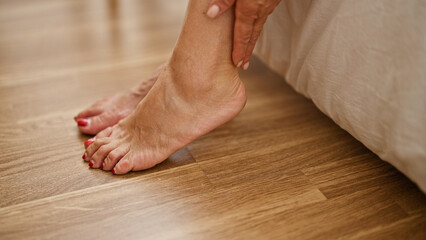 Middle age hispanic woman sitting on bed massaging feet at bedroom