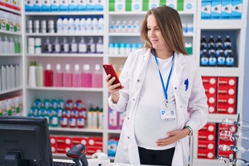 Young pregnant woman pharmacist using smartphone working at pharmacy
