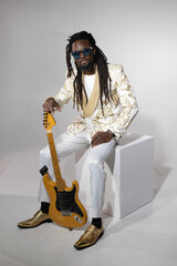 portrait of a stylish African man in a white suit and sunglasses with an electric guitar